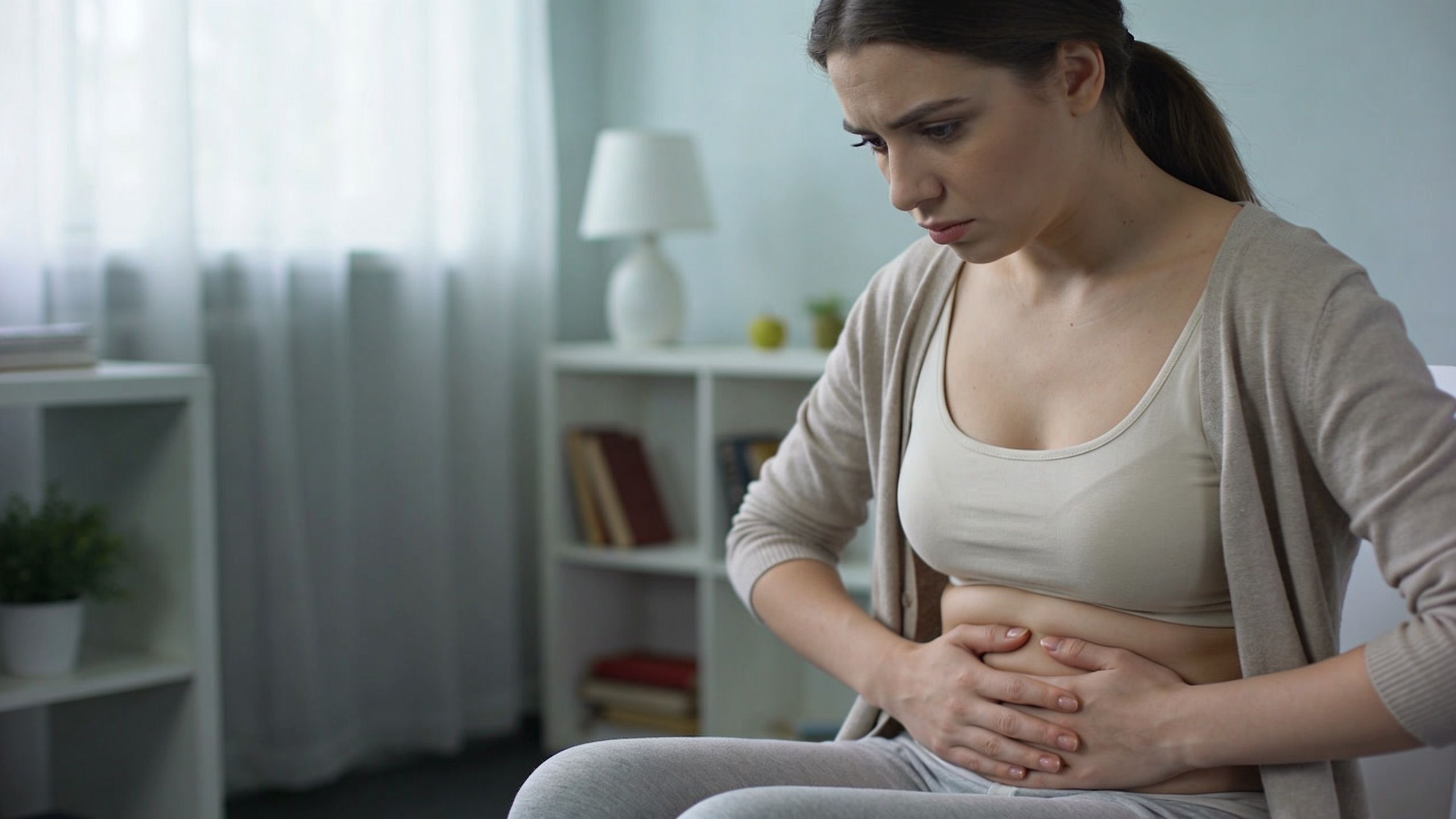 A young woman feeling discomfort while holding her stomach, representing common digestive health issues.